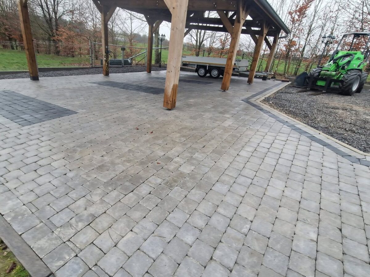 Cour en pavés béton sous un grand abri ouvert, avec accès en empierrement