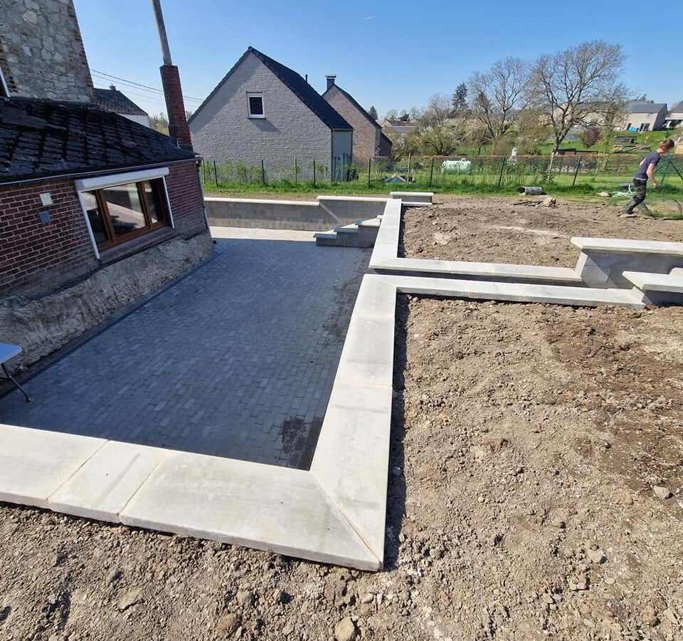 Mur de soutènement en blocs à bancher ferraillés et terrasse en pavés béton en cours de pose